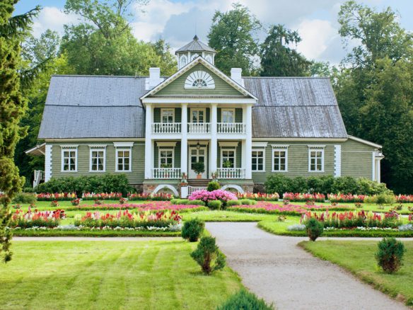A large green house with many flowers in the front yard.